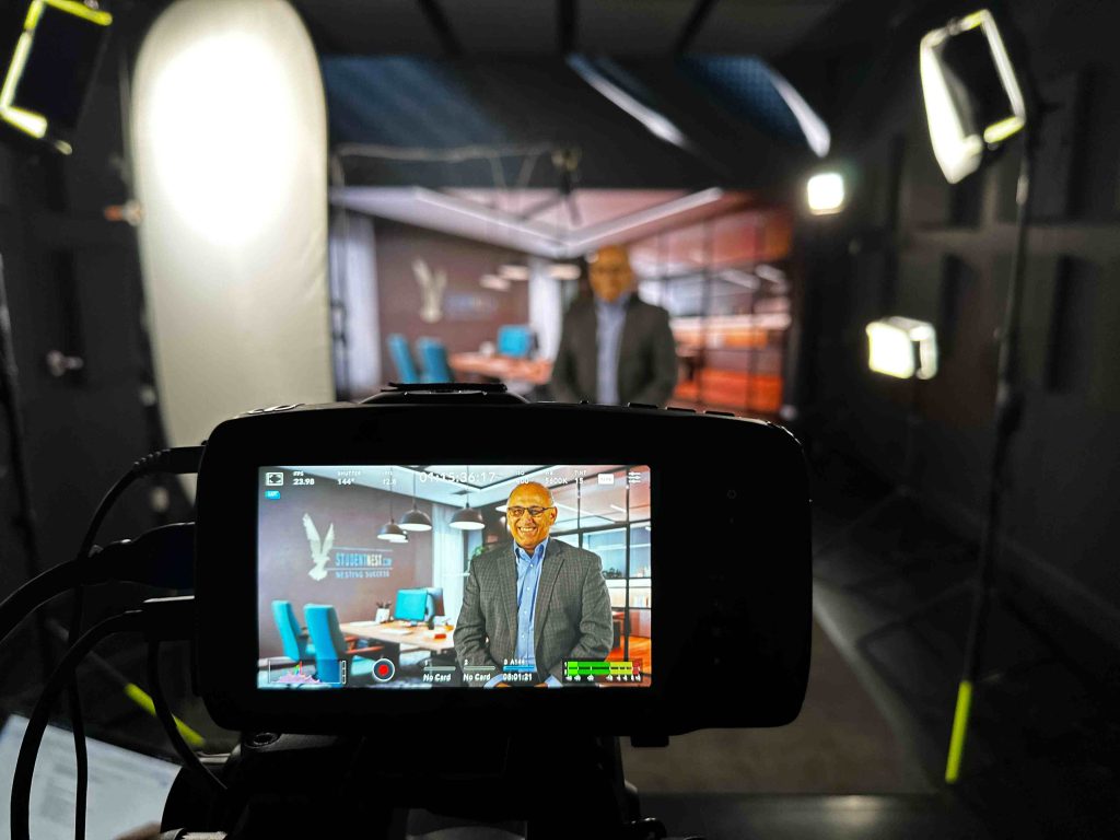 Chander Joshi appearing through a camera monitor during an interview at a television studio