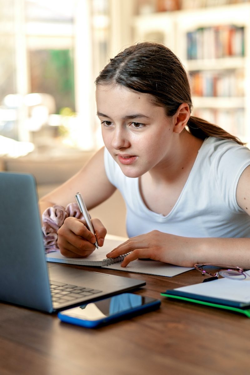 Teenager girl studying online at home looking at laptop at  quarantine isolation period during pandemic. Home schooling. Social distancing. Online school test.