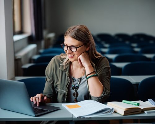 Young happy woman using laptop while e-learning in lecture hall.